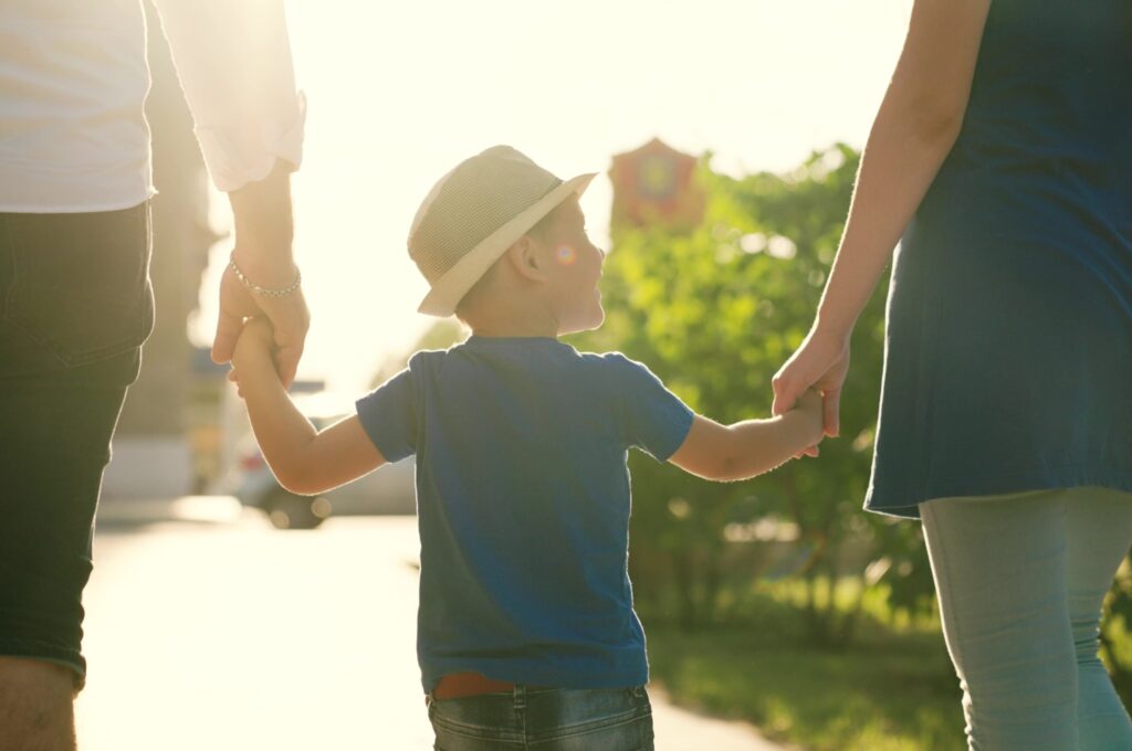 A family with a young child holding hands outdoors.